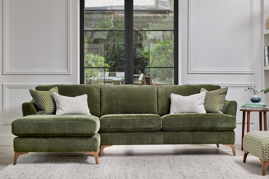 Green sectional sofa in a living room with large windows.