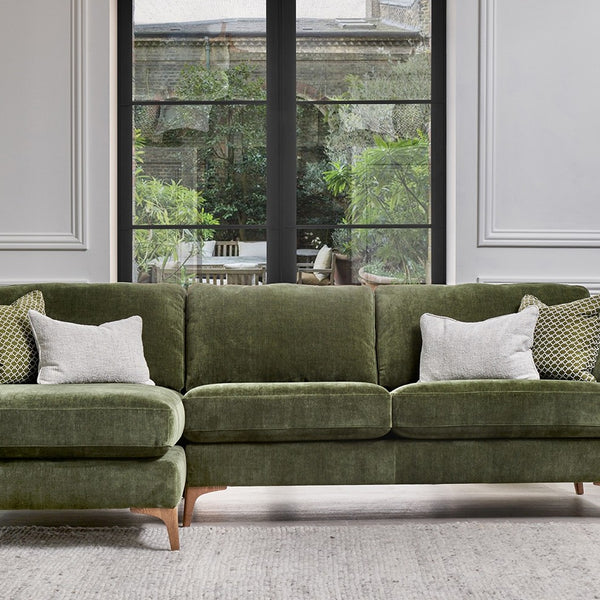 Green sectional sofa in a living room with large windows.