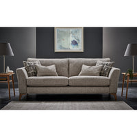 A modern two-seater sofa in textured beige fabric, styled with four matching throw pillows and two patterned accent pillows, set in a contemporary living room with dark grey walls, wooden side tables, lamps, and a rug.