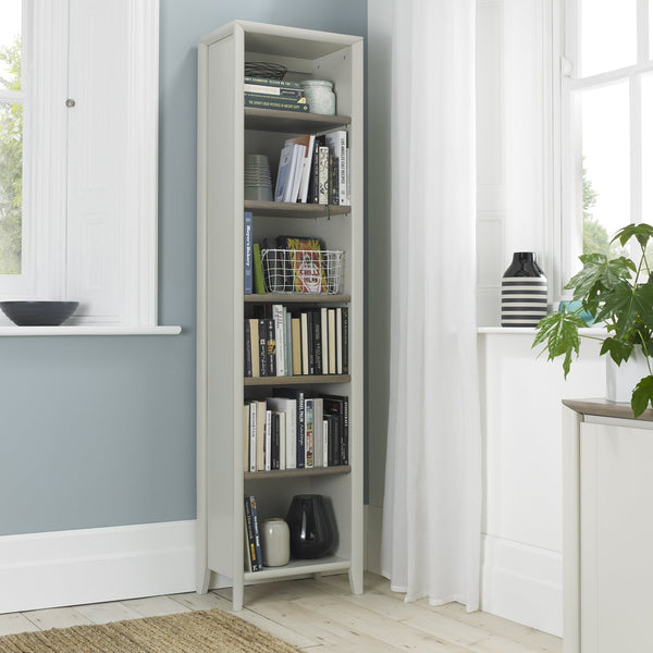Tall bookshelf filled with books and decorative items in a room with windows and plants.