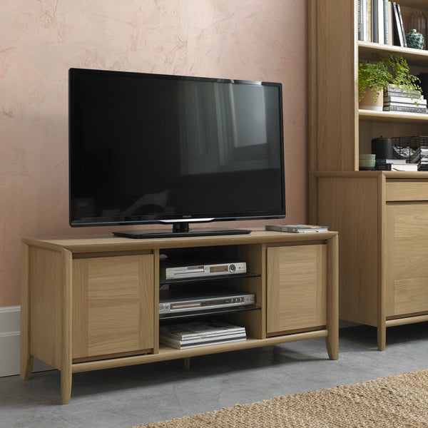 Wooden TV stand with a television and electronic devices against a pink wall.