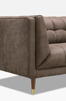 A close-up of a modern upholstered sofa in taupe brown leather, showing the armrest, tufted back cushions, and a tapered wooden leg with a gold metal cap, set against a white background.