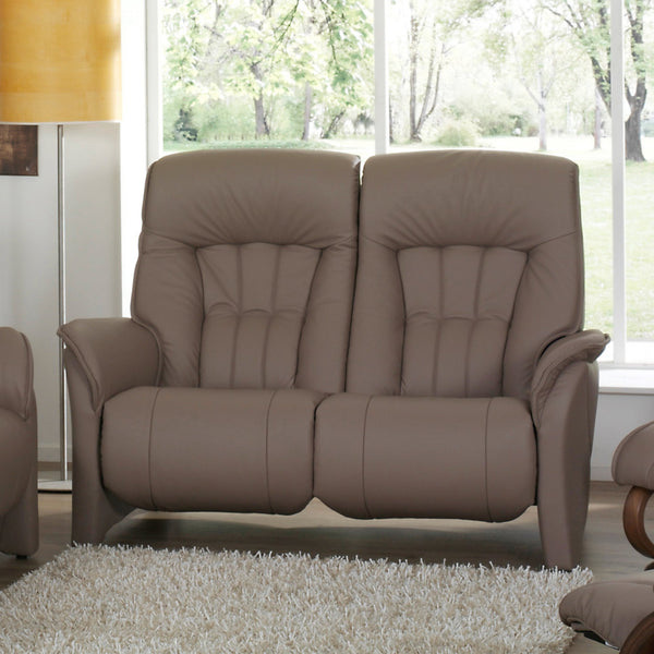 Brown leather sofa in a living room with large windows and a lamp.