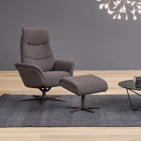 Grey recliner chair with stool on a wooden floor against a grey wall.