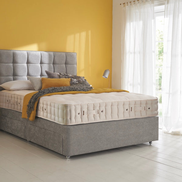 Grey upholstered bed with tufted headboard in a bright room with yellow walls and white curtains.
