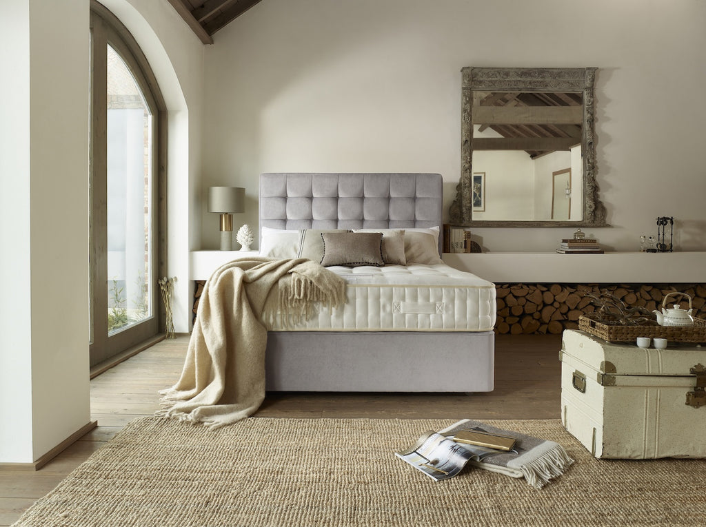 Modern bedroom with a grey upholstered bed, wooden floor, and large mirror.
