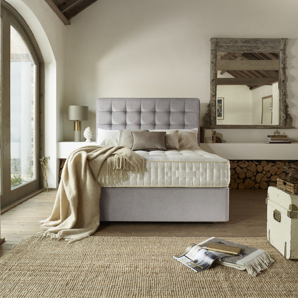 Modern bedroom with a grey upholstered bed, wooden floor, and large mirror.