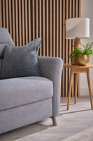 Grey armchair in a living room with a side table and lamp in the background.