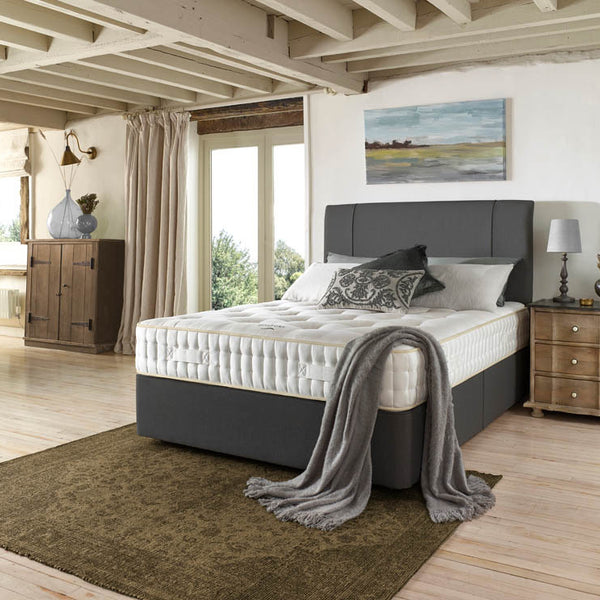 Bedroom with a bed featuring a grey headboard and white mattress, surrounded by wooden furniture and decor.