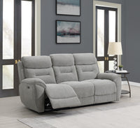 Grey recliner sofa in a living room with large windows and framed pictures on the wall.
