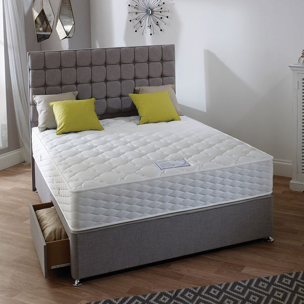 Bed with white mattress, grey headboard, and green pillows in a bedroom setting.