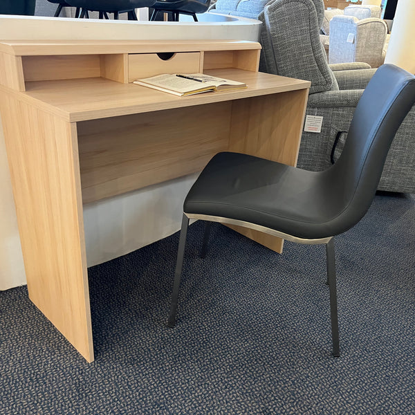 Small wooden desk with a black chair in a showroom setting