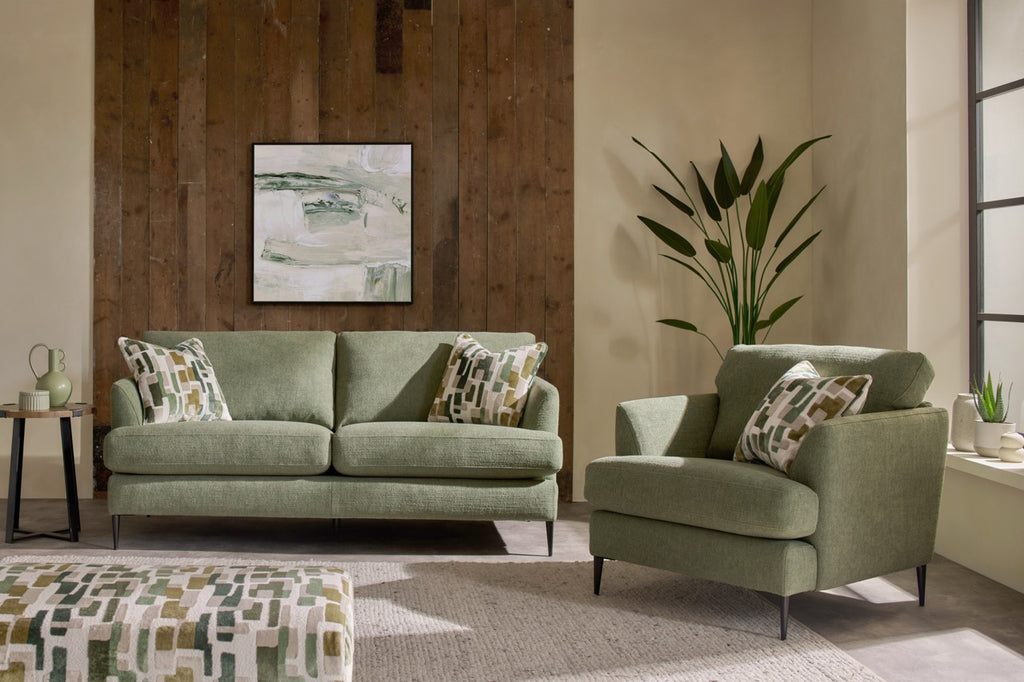 Green sofa and armchair in a living room with a wooden wall and plant.
