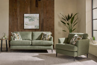 Green sofa and armchair in a living room setting with a plant and abstract painting.