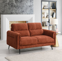 Rust sofa in a living room setting with a fireplace and shelves.