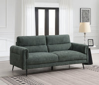 Green sofa in a room with a lamp and framed picture on a white wall.