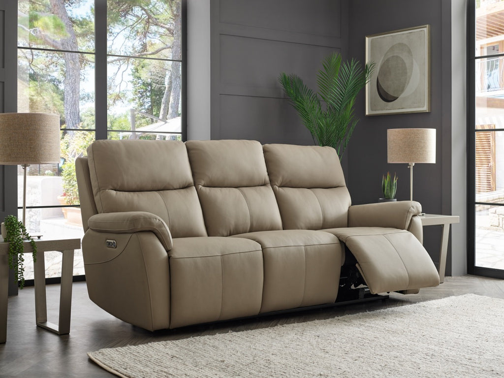 Beige reclining sofa in a living room setting with large windows and a plant.