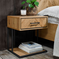 Wooden nightstand with a drawer, books, and a candle next to a bed.