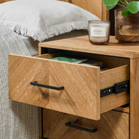 Wooden nightstand with open drawer, candle, and plant in a bedroom setting.