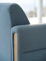 Close-up of a blue upholstered chair with wooden armrest.