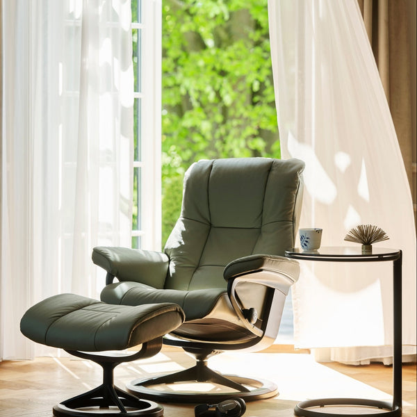 Modern green armchair with stool in a bright room with large windows.