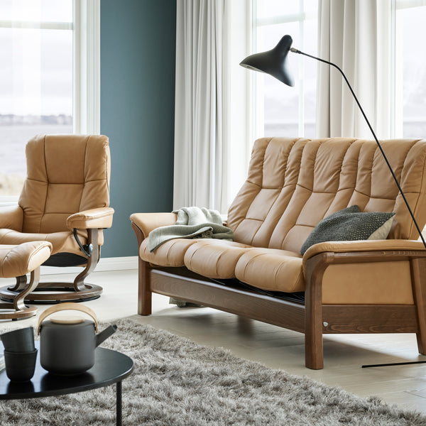 Taupe sofa and armchair in a living room with large windows and a lamp.