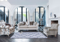 A styled living room featuring a cream-coloured sofa, a patterned armchair, a striped armchair, a geometric area rug, and a white fireplace mantel against a background of white arched windows.