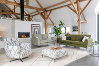 Modern living room with green sofas, white armchair, and wooden beams.