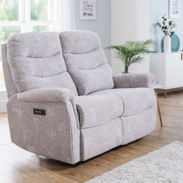 Grey recliner sofa in a living room setting with a rug and window in the background.
