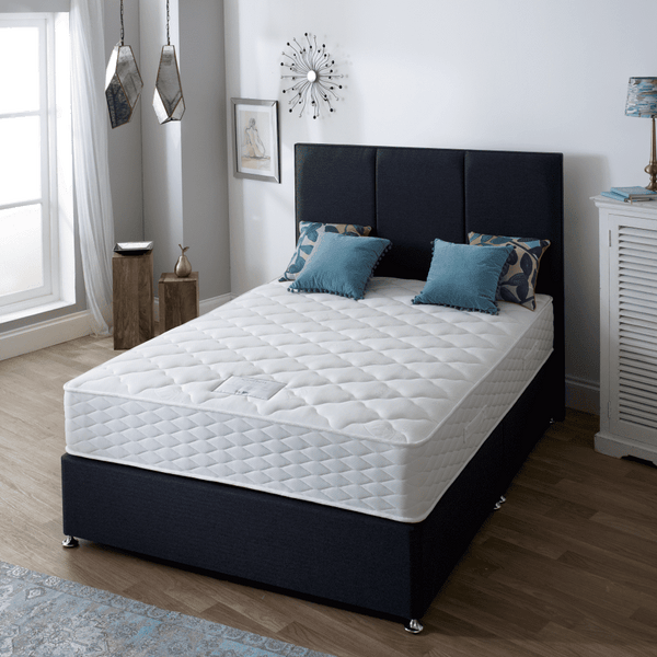 Bedroom with a bed featuring a white mattress and blue pillows, next to a white cabinet.