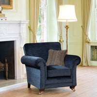 Blue armchair with a striped pillow in a living room setting with a fireplace and lamp.