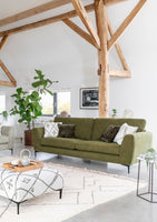 Green sofa in a modern living room with wooden beams and a white rug.