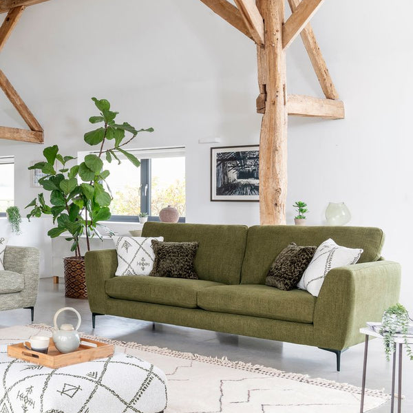 Green sofa in a modern living room with wooden beams and a white rug.